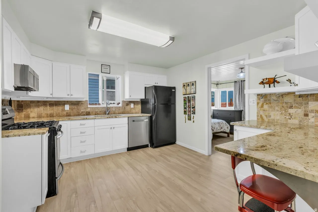 Kitchen featuring tasteful backsplash, light stone countertops, stainless steel appliances, and white cabinetry
