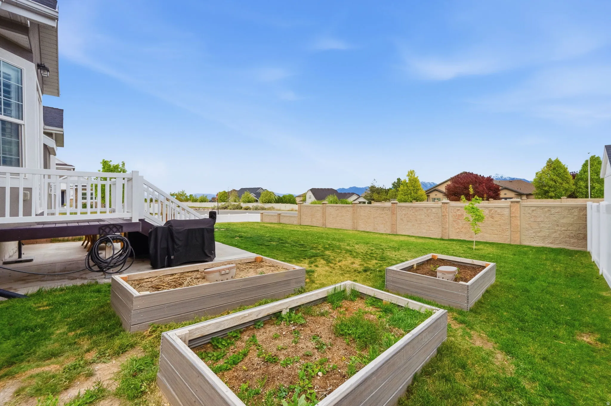 Fenced backyard featuring a patio area, a deck, and a vegetable garden