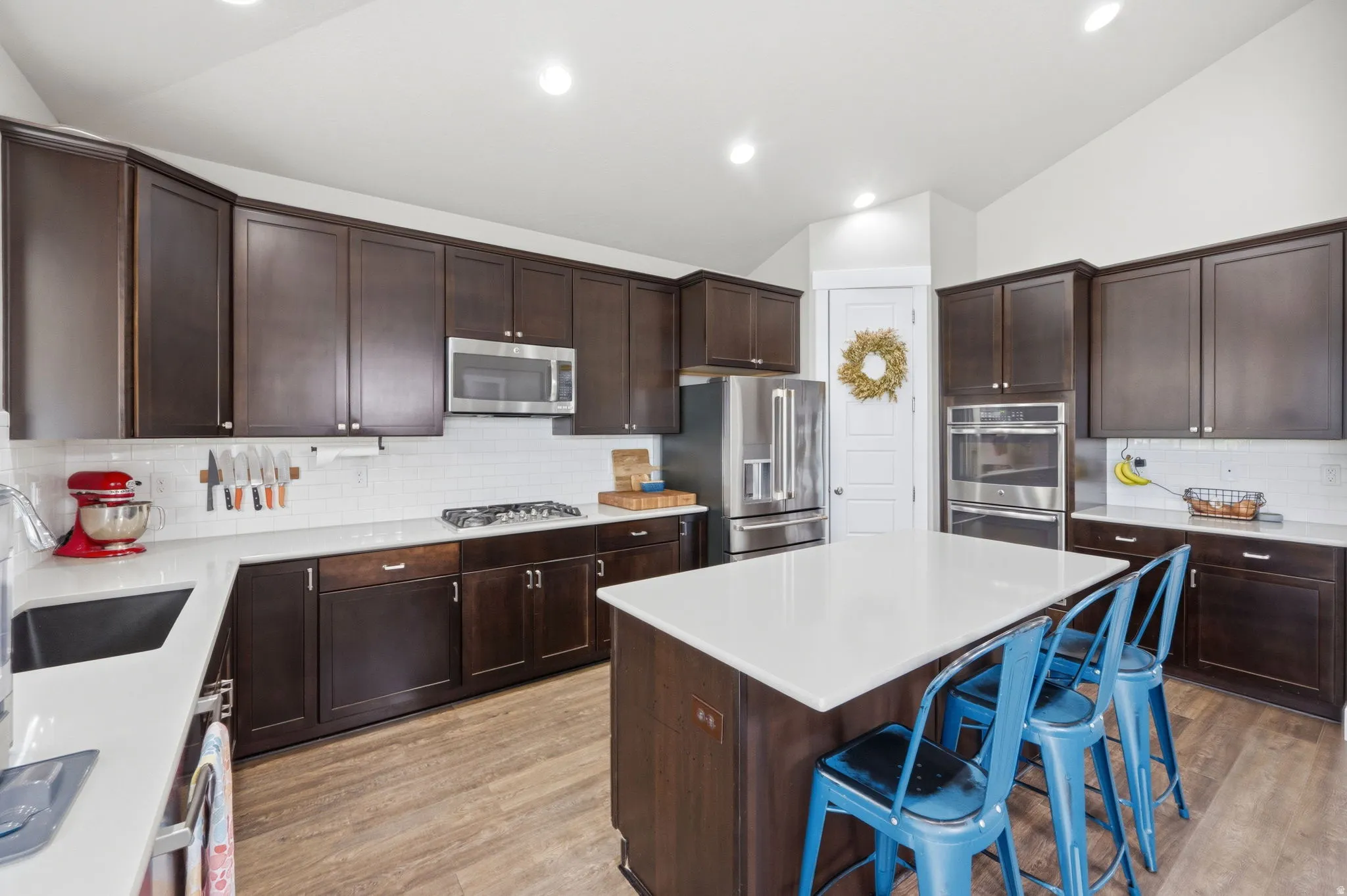 Kitchen with lofted ceiling, dark wood finish cabinetry, a kitchen island, stainless steel appliances, and a kitchen breakfast bar
