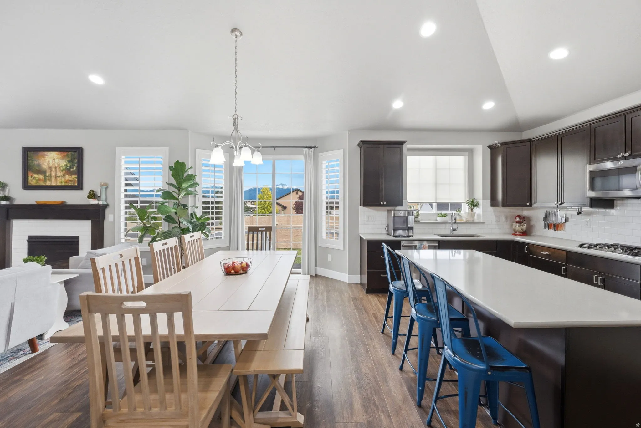 Dining space with dark wood-type flooring, a fireplace, hanging lights, and vaulted ceiling