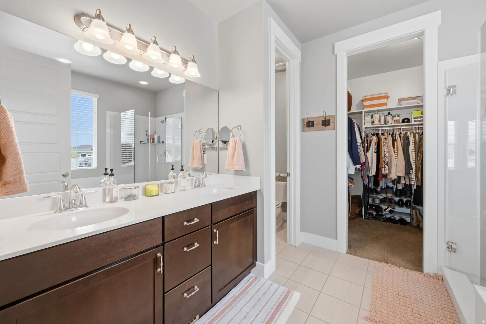 Full bath featuring a shower stall, double vanity, a walk in closet, and light tile patterned flooring