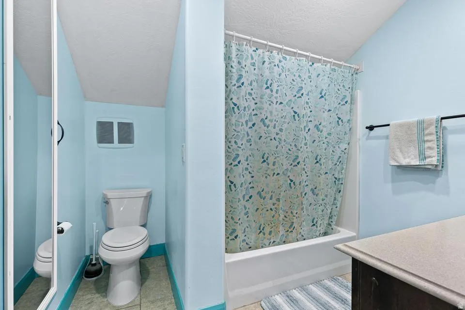 Full bathroom with a textured ceiling, vanity, shower / bath combo with shower curtain, and light tile patterned flooring