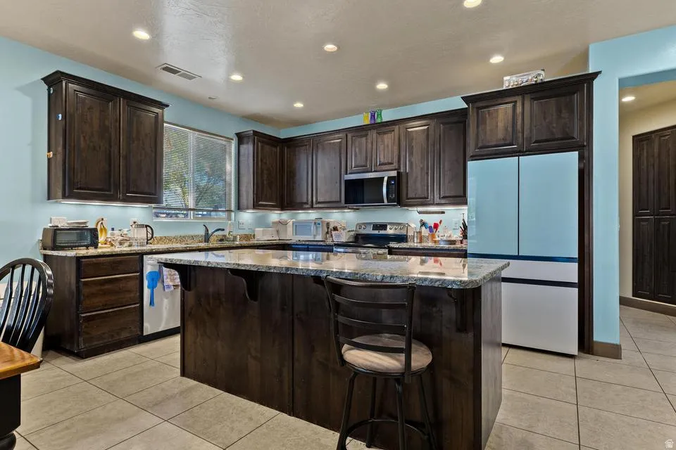 Kitchen with dark wood finish cabinetry, stainless steel appliances, a breakfast bar, and recessed lighting