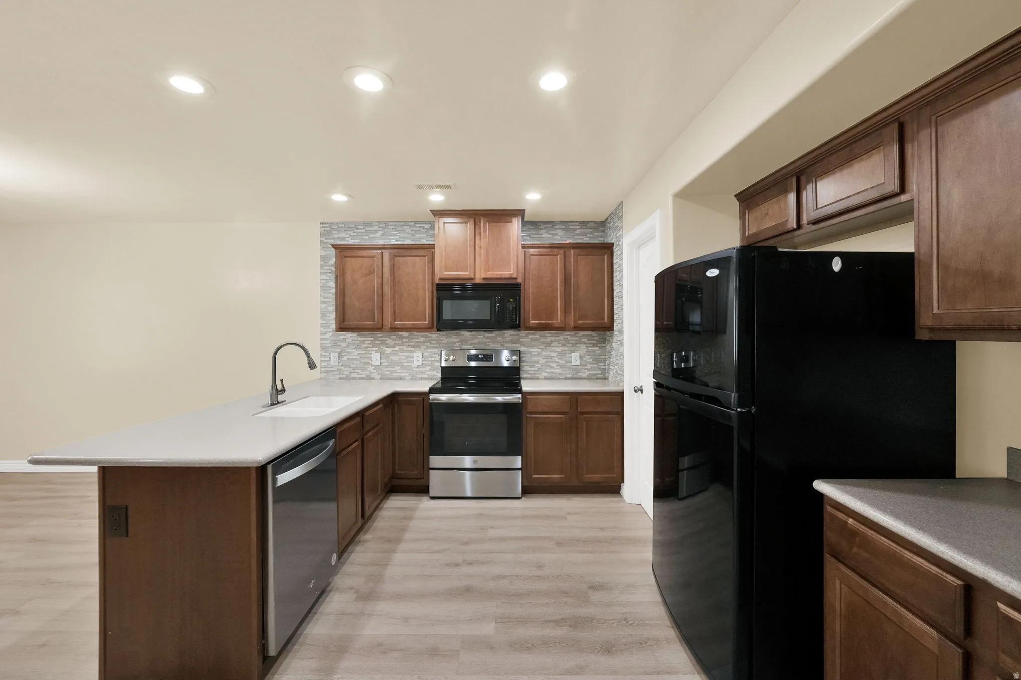 Kitchen featuring black appliances, a peninsula, tasteful backsplash, light wood-type flooring, and recessed lighting