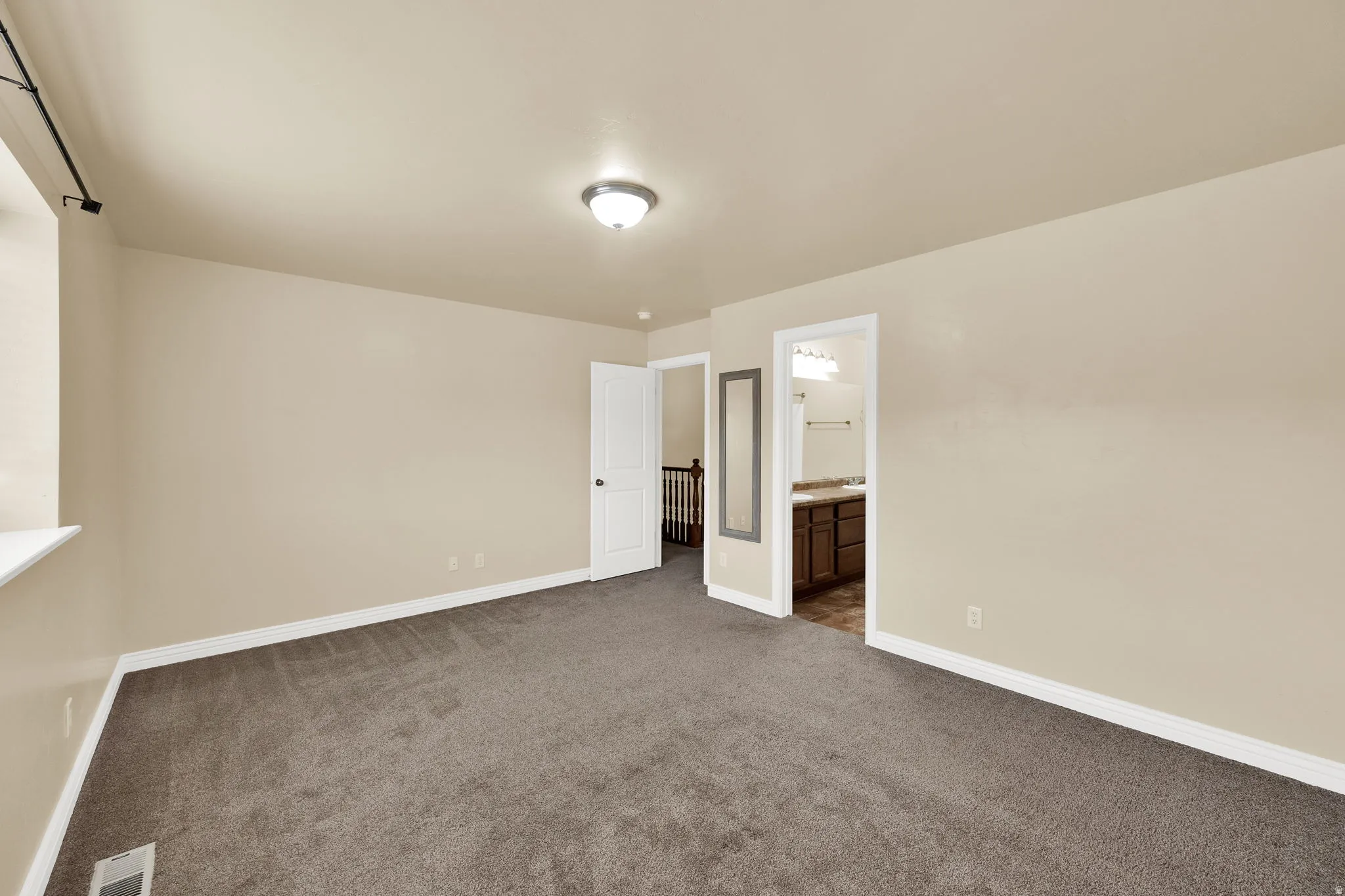 Unfurnished bedroom featuring dark carpet and ensuite bath