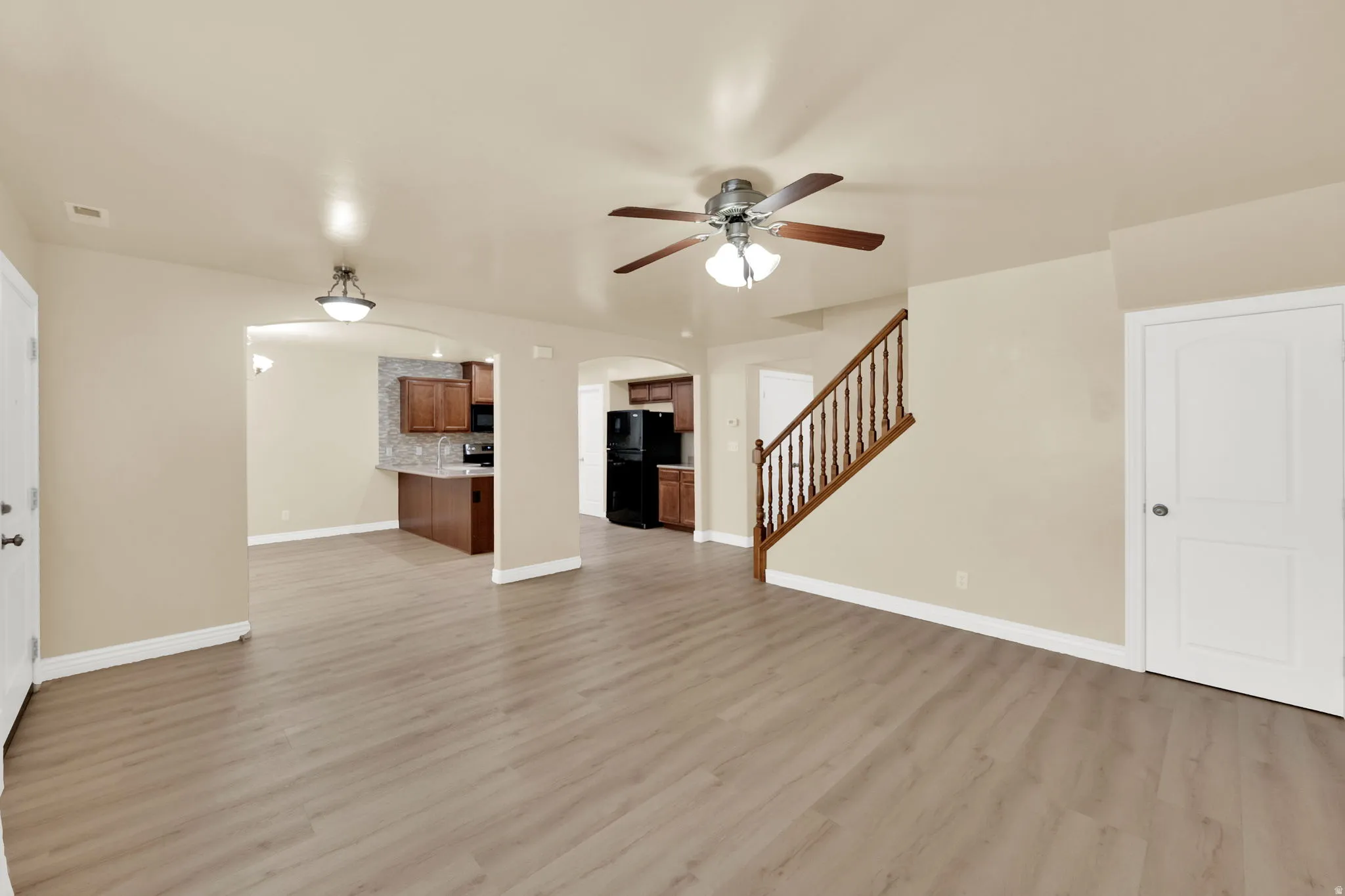 Unfurnished living room with arched walkways, ceiling fan, and light wood-type flooring