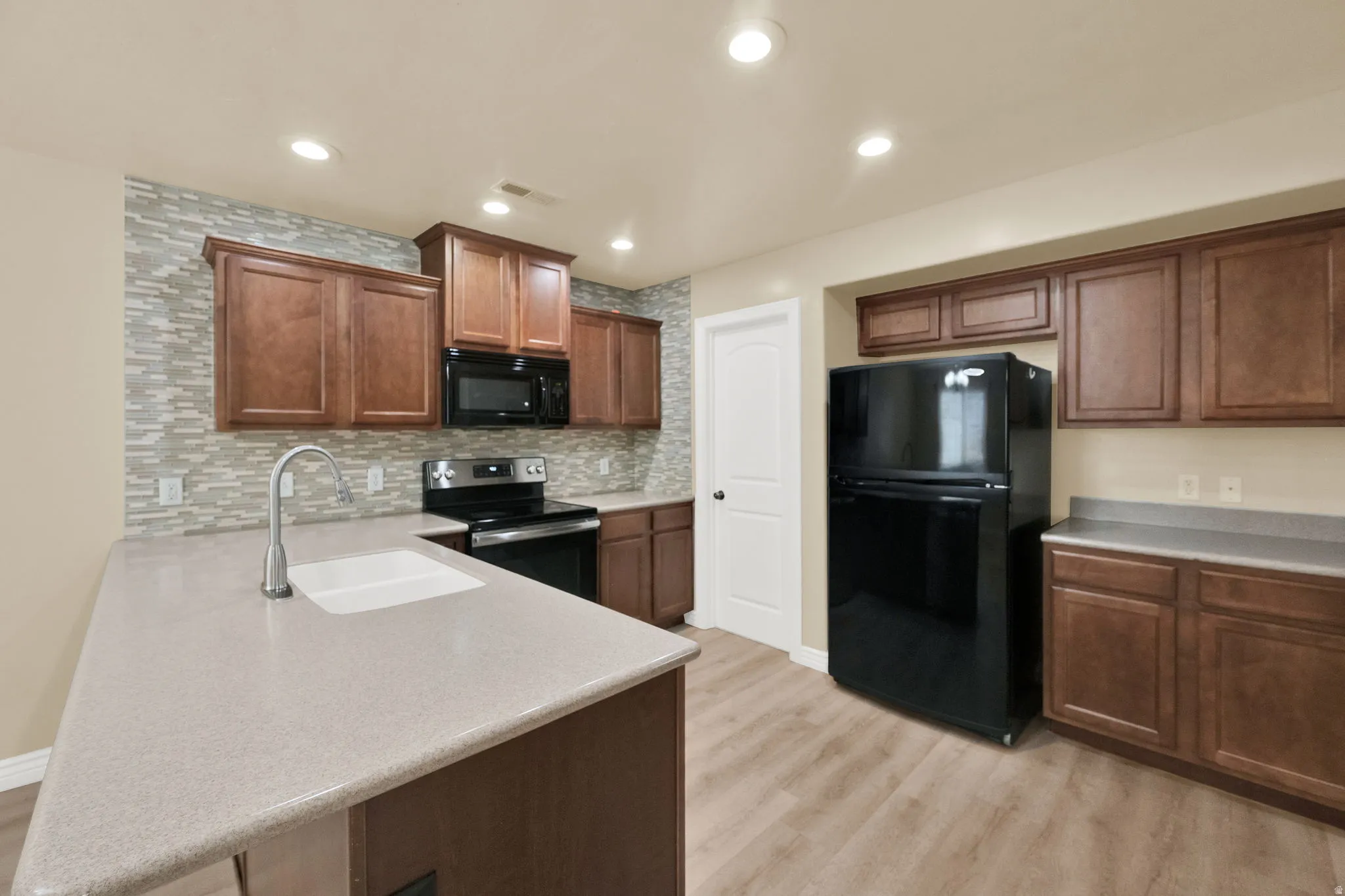 Kitchen featuring black appliances, a peninsula, decorative backsplash, light wood-style flooring, and recessed lighting