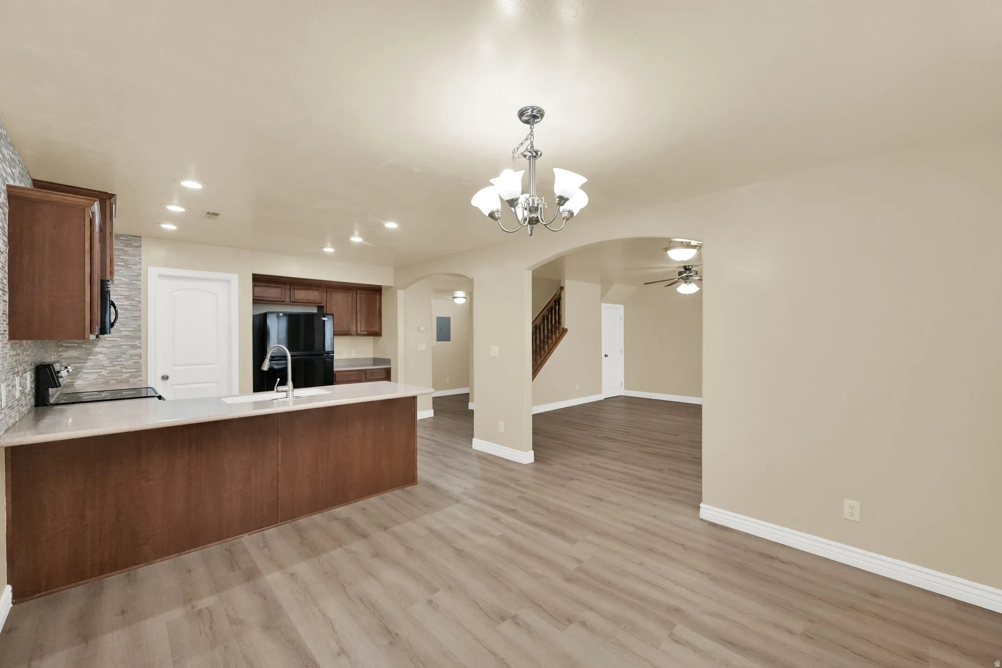 Kitchen featuring suspended lighting, arched walkways, a peninsula, black appliances, and light wood-type flooring
