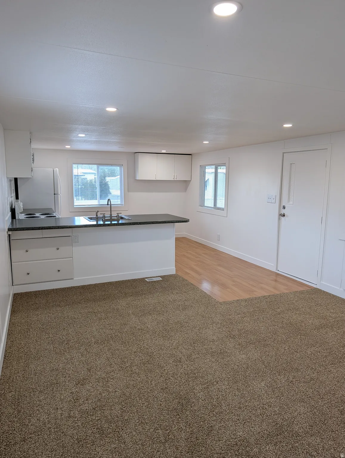 Kitchen with white cabinetry, dark countertops, light colored flooring, freestanding refrigerator, and plenty of natural light