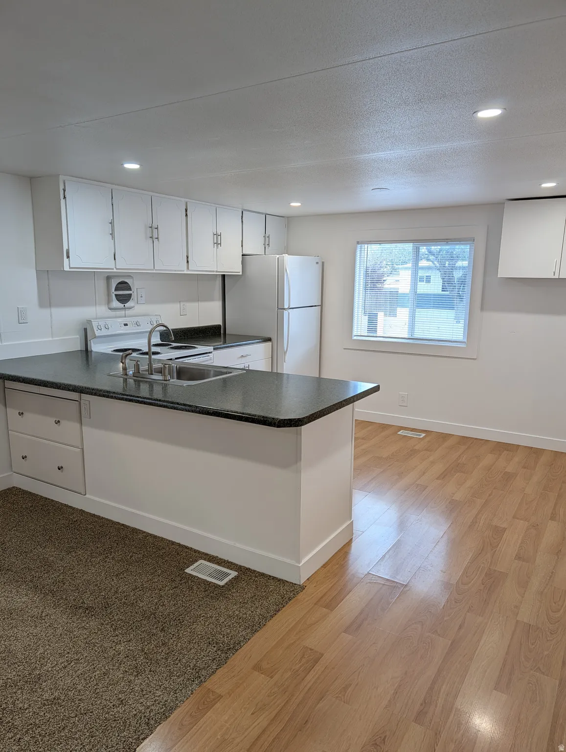 Kitchen featuring white cabinetry, a peninsula, white appliances, dark countertops, and light wood-style flooring