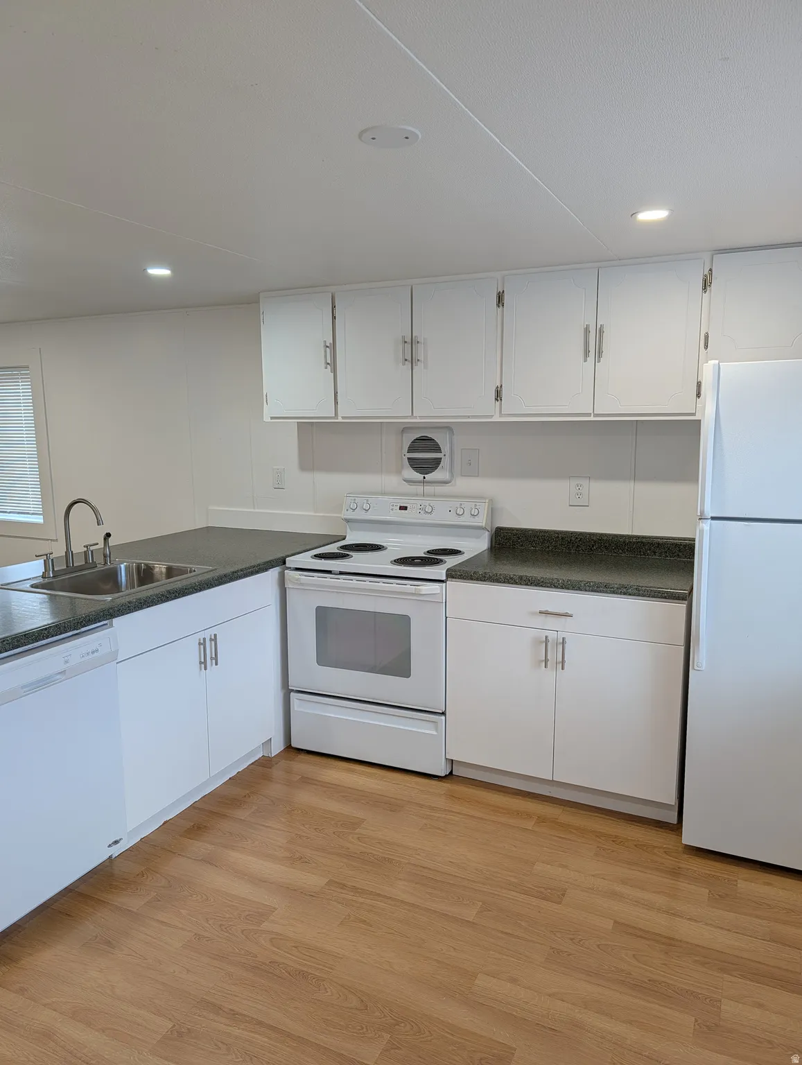 Kitchen featuring dark countertops, white appliances, white cabinetry, light wood-style flooring, and recessed lighting