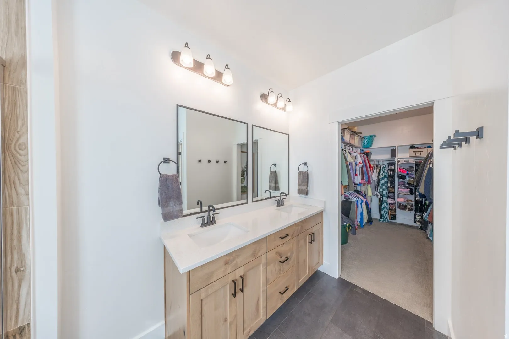 Full bathroom featuring double vanity, a walk in closet, dark colored carpet, and dark tile patterned floors