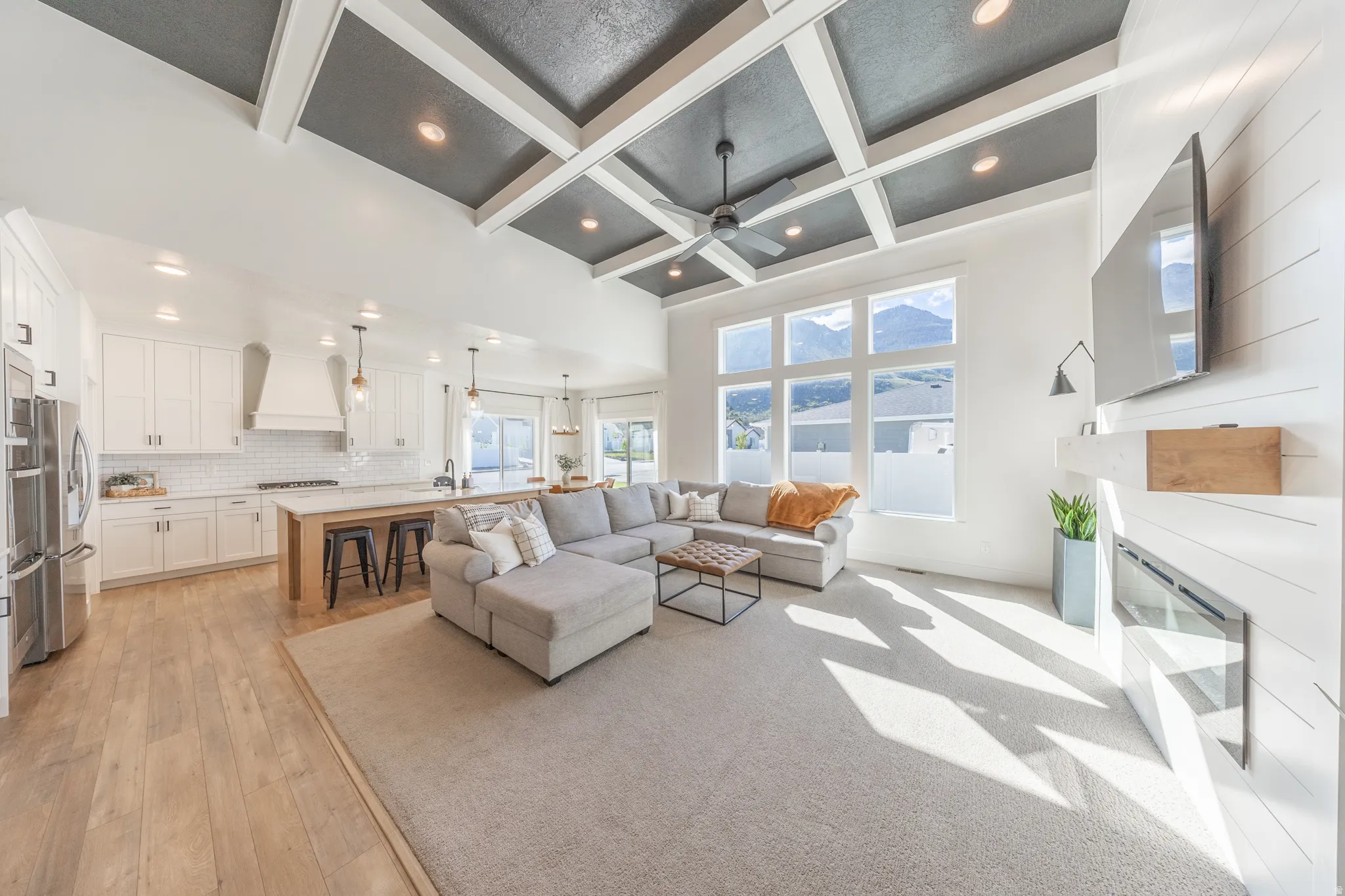 Living room with coffered ceiling, a glass covered fireplace, ceiling fan, light wood-type flooring, and recessed lighting