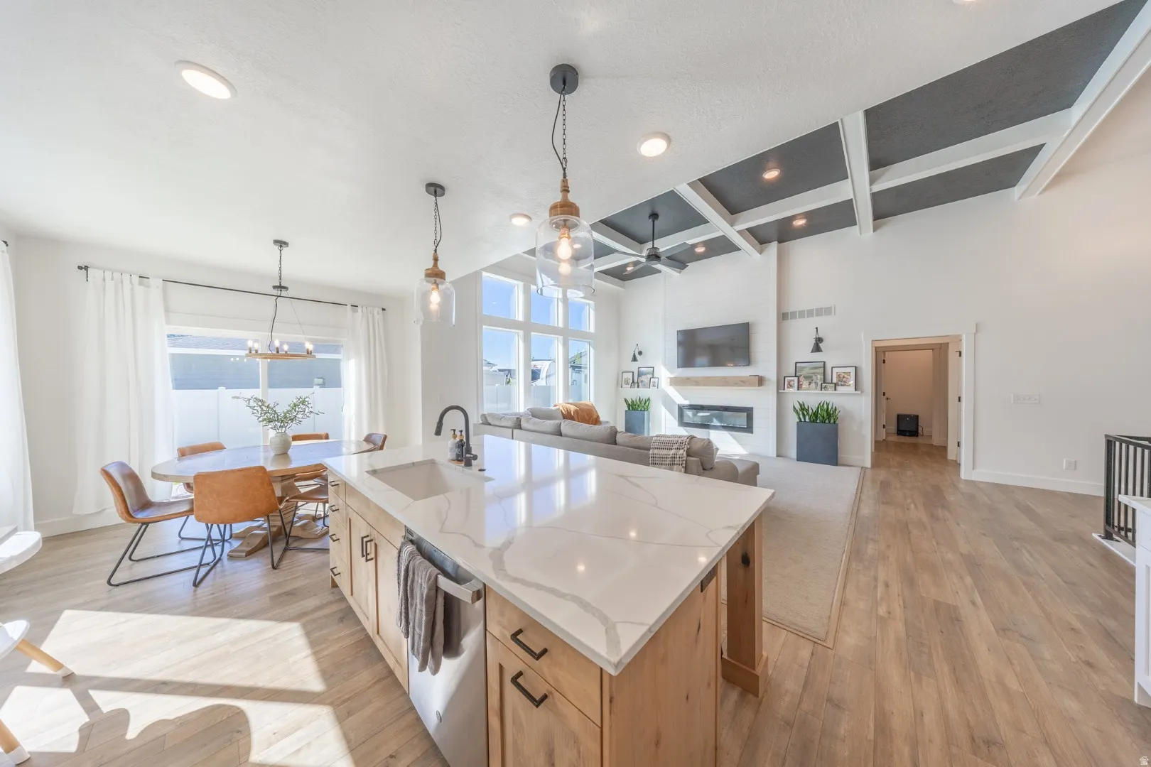 Kitchen with coffered ceiling, light wood-type flooring, a center island with sink, light stone countertops, and open floor plan