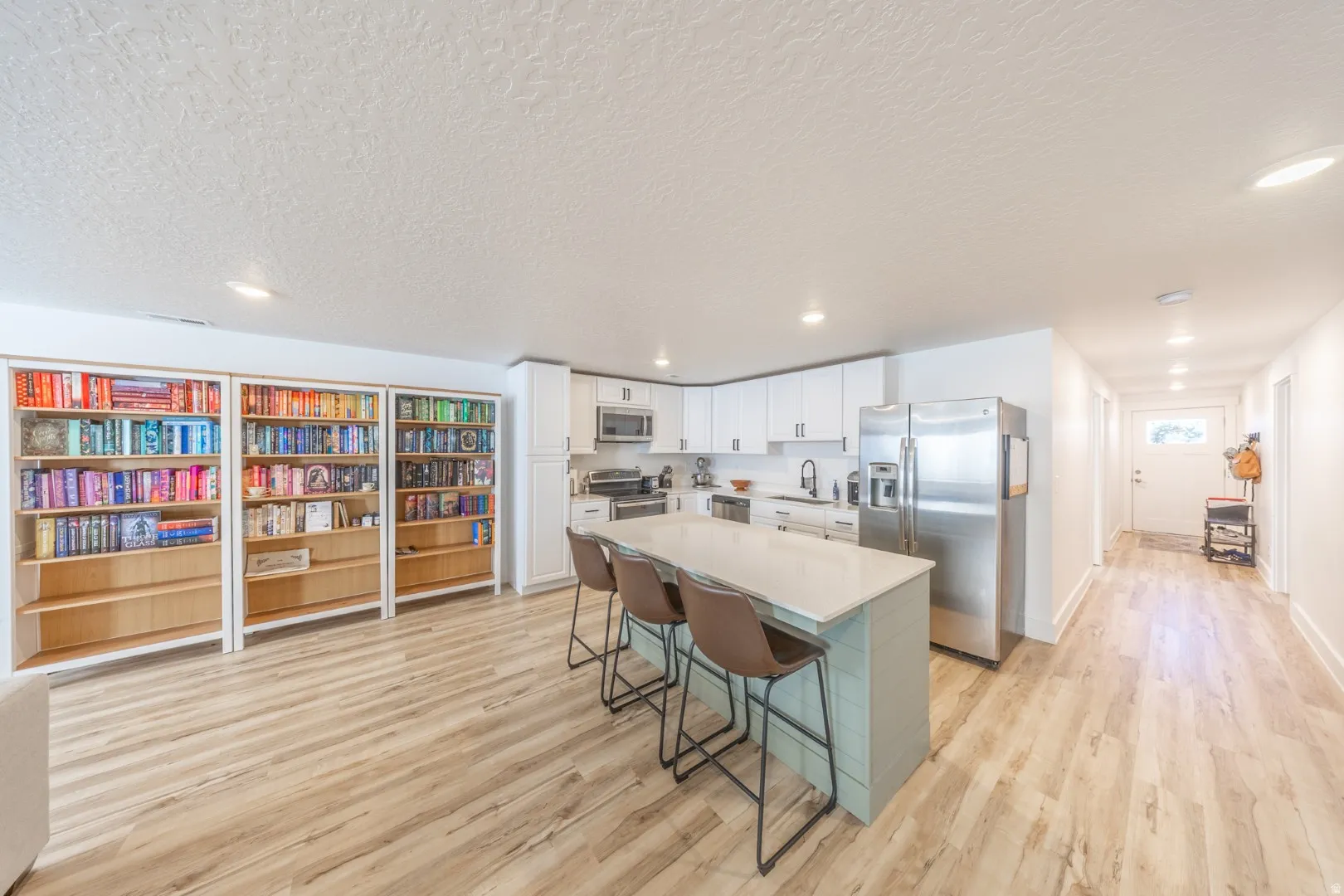 Kitchen with stainless steel appliances, a breakfast bar, white cabinets, a center island, and light wood finished floors