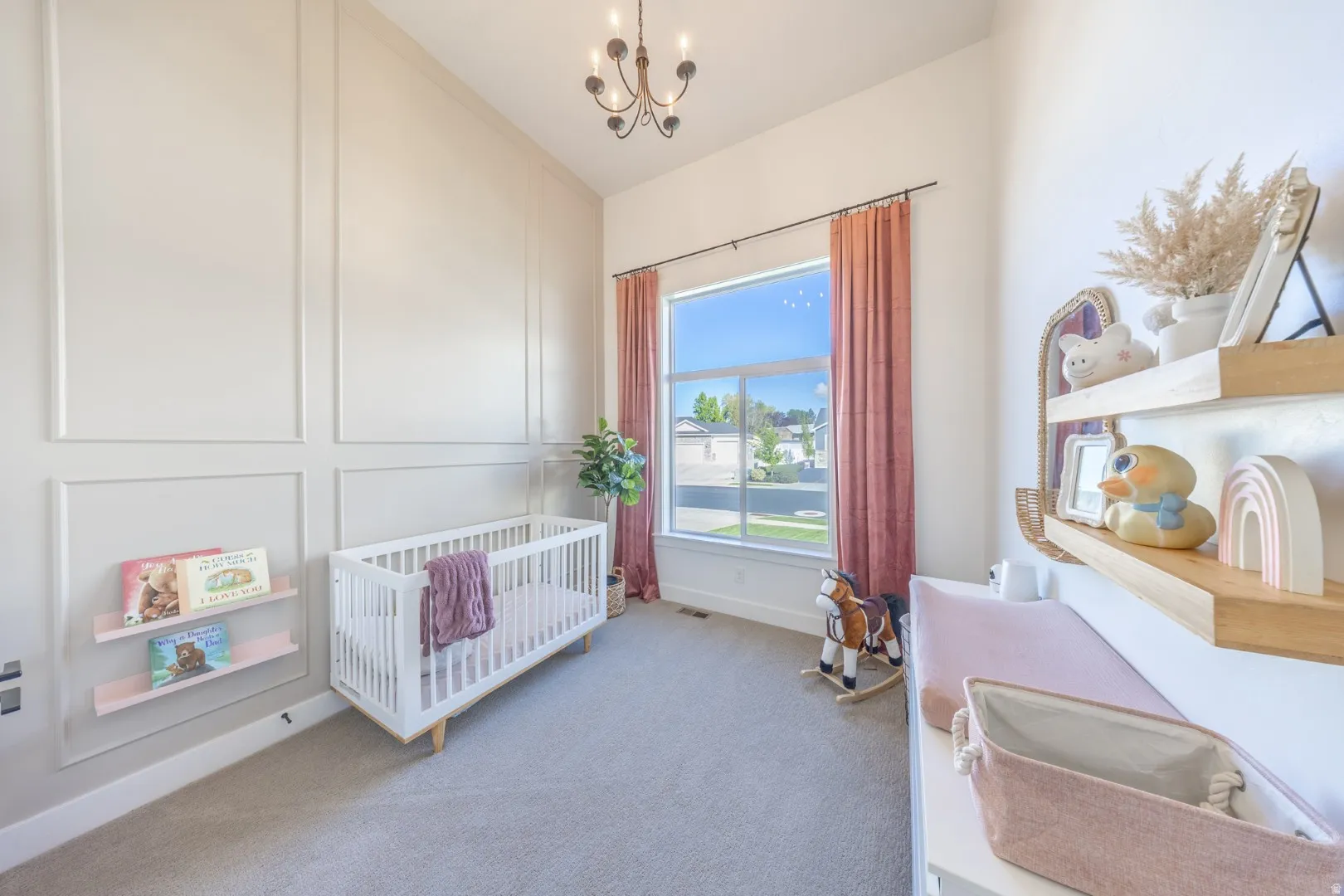 Bedroom featuring a crib, light colored carpet, a chandelier, vaulted ceiling, and a decorative wall
