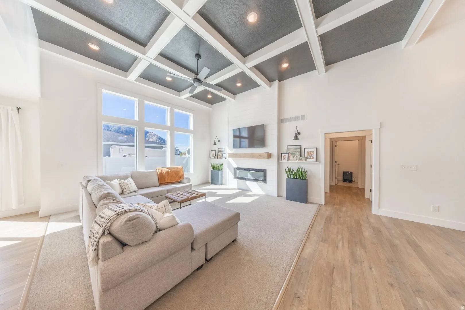 Living room with light wood-style floors, coffered ceiling, a large fireplace, and a ceiling fan