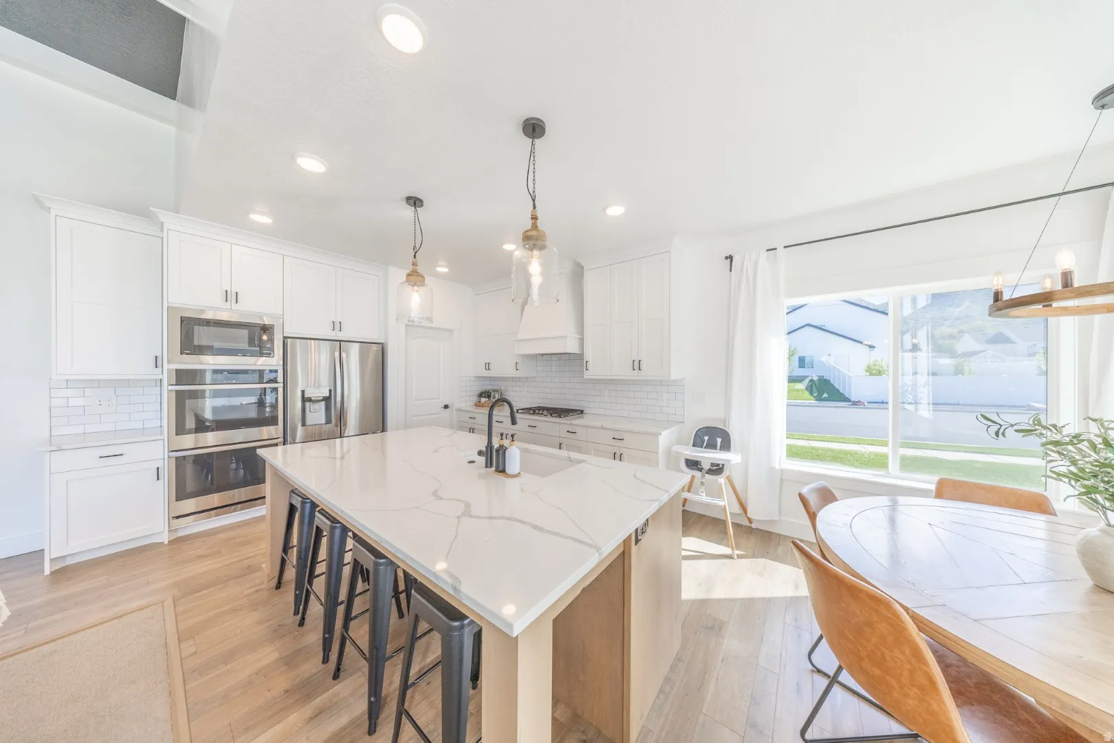 Kitchen with light wood-style flooring, a large island, a kitchen breakfast bar, stainless steel appliances, and light stone counters