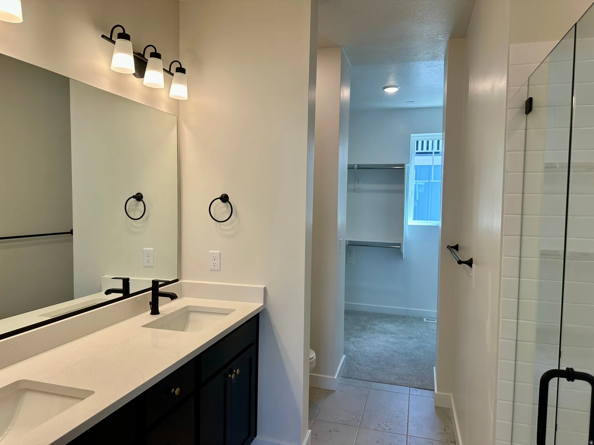 Owner's bathroom with double vanity, a spacious closet, upgraded shower, and floor tile
