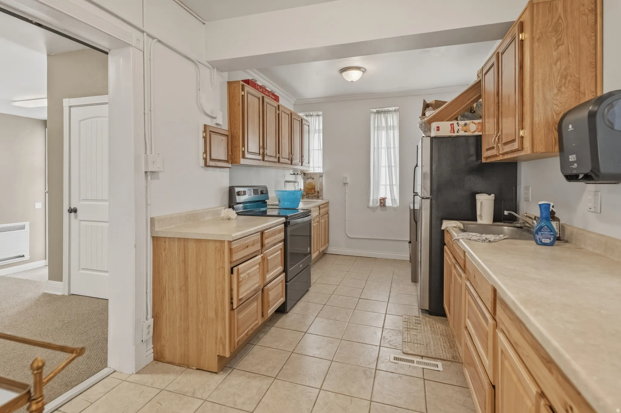 Kitchen featuring stainless steel appliances, light countertops, light tile patterned floors, ornamental molding, and light carpet