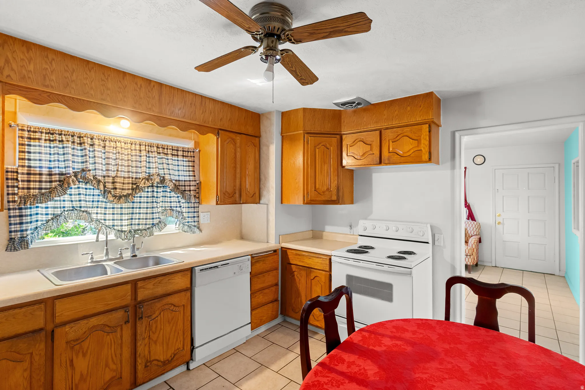 Kitchen with light countertops, white appliances, light tile patterned floors, ceiling fan, and wood finish cabinetry