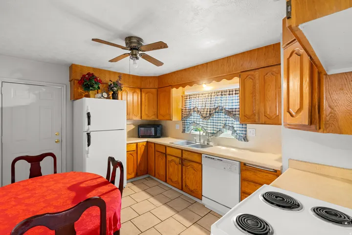 Kitchen with white appliances, light countertops, wood finish cabinetry, exhaust hood, and a ceiling fan