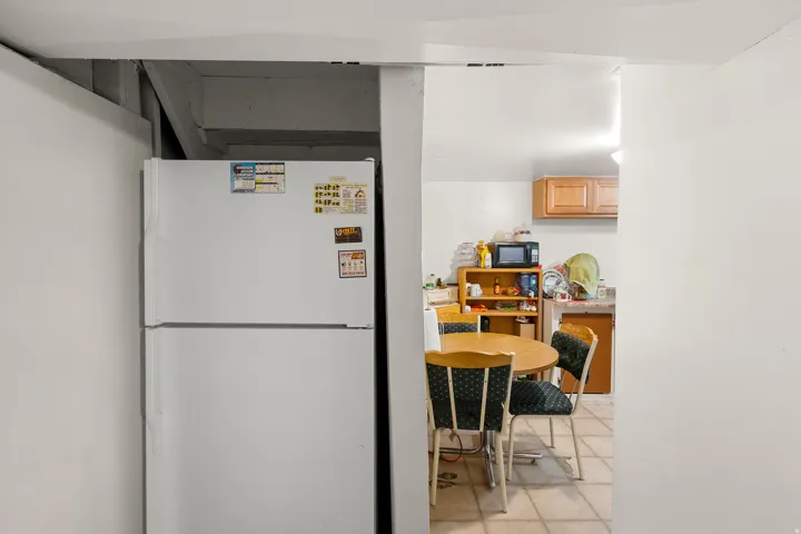 Kitchen with freestanding refrigerator, light wood finish cabinets, black microwave, and light tile patterned floors
