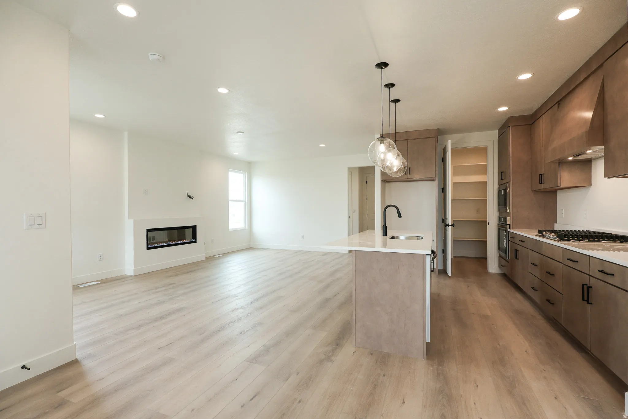 Kitchen featuring open floor plan, a kitchen island with sink, hanging light fixtures, light stone counters, and a glass covered fireplace