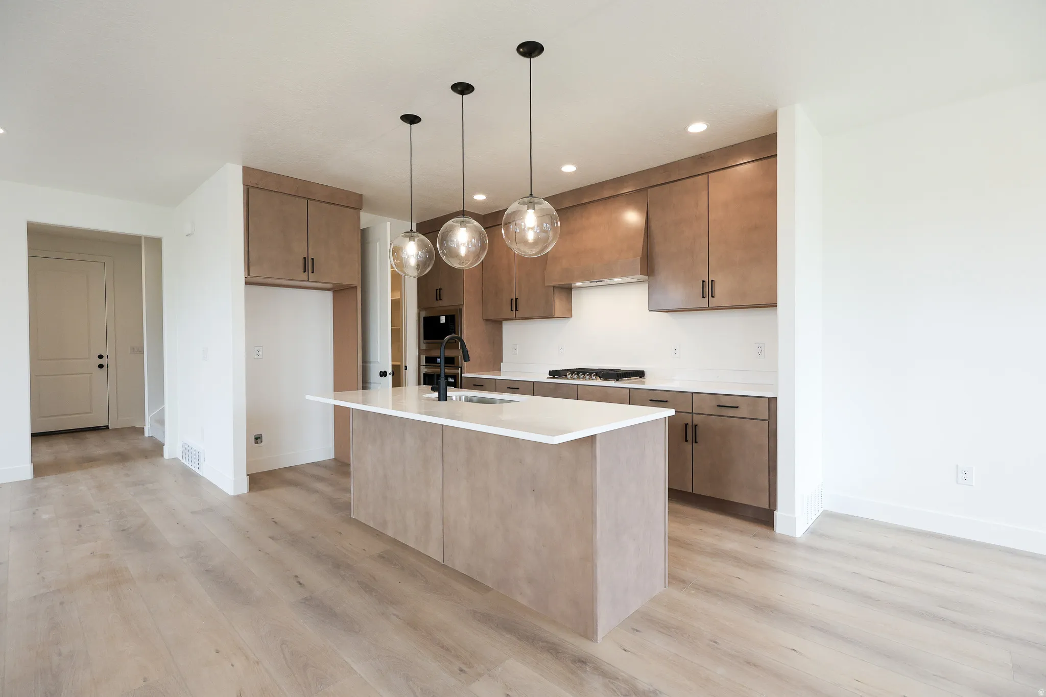Kitchen featuring light wood finished floors, a kitchen island with sink, hanging light fixtures, stainless steel gas cooktop, and light stone countertops