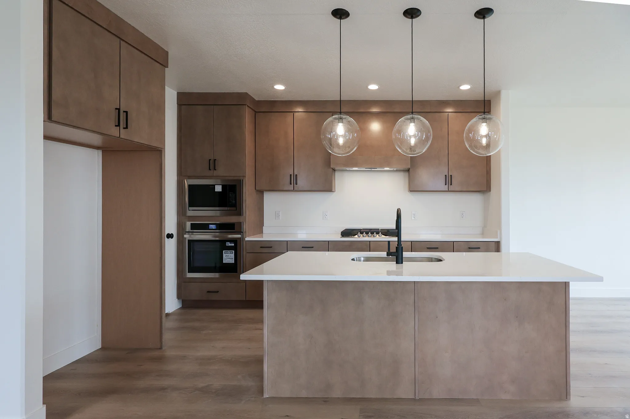 Kitchen with stainless steel appliances, pendant lighting, a center island with sink, dark wood-type flooring, and light stone counters