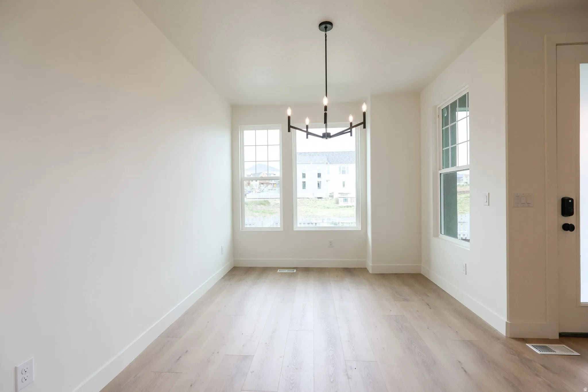 Unfurnished dining area with a chandelier, light wood-style floors, and healthy amount of natural light