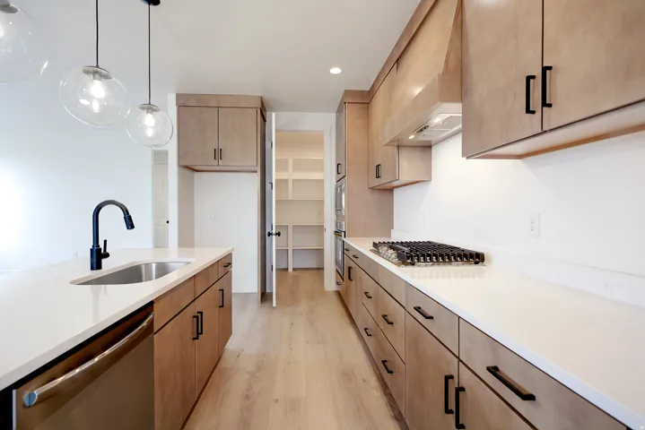 Kitchen featuring stainless steel appliances, light stone counters, light wood-style flooring, decorative light fixtures, and light wood finish cabinets