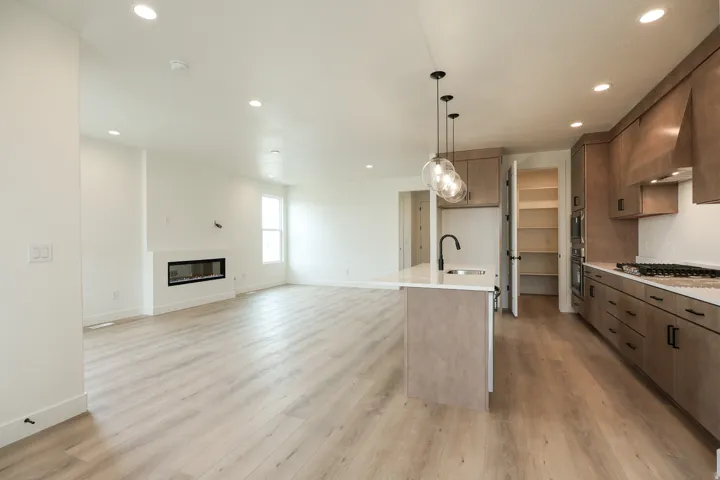 Kitchen featuring open floor plan, a kitchen island with sink, hanging light fixtures, light stone counters, and a glass covered fireplace