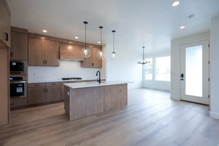 Kitchen with hanging lights, an island with sink, stainless steel appliances, light wood-style floors, and open floor plan