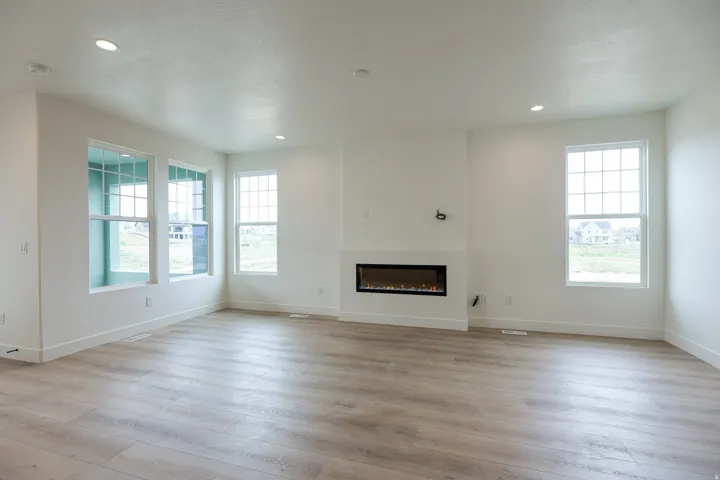 Unfurnished living room with a glass covered fireplace, light wood-style floors, healthy amount of natural light, and recessed lighting