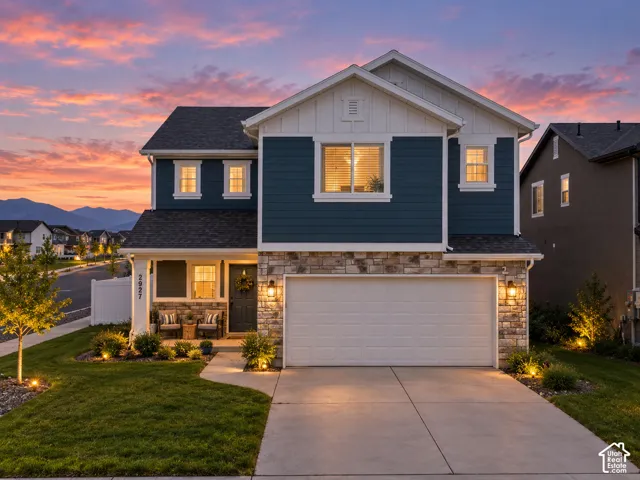 Two-story residence featuring a two-car garage, stone and siding exterior, and a covered front porch