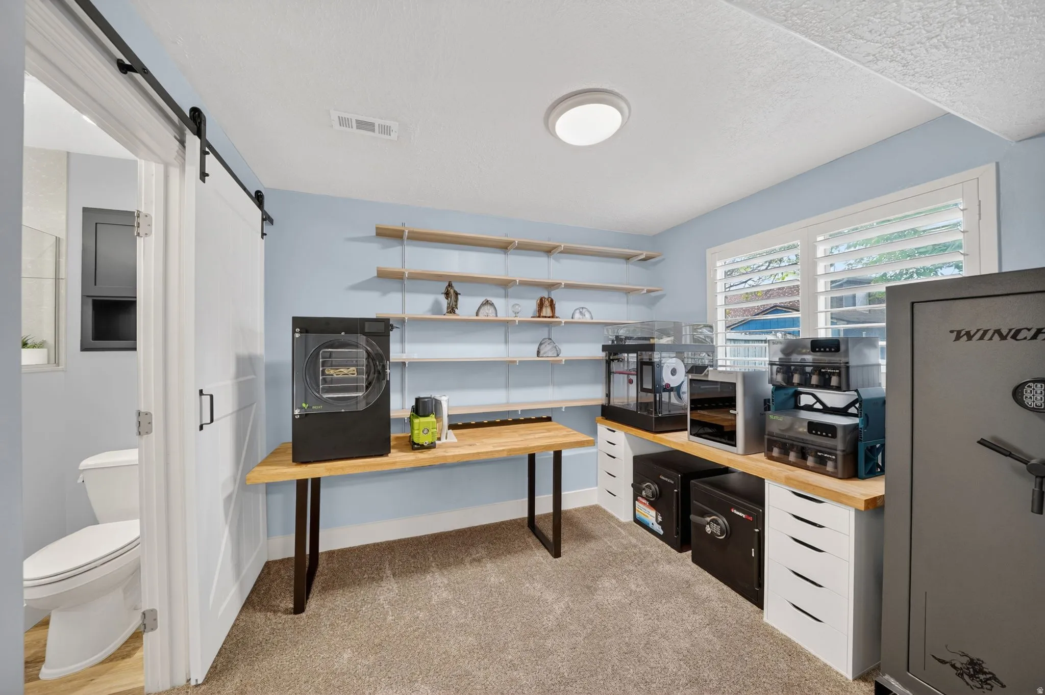 Home office featuring a barn door, light carpet, and a textured ceiling