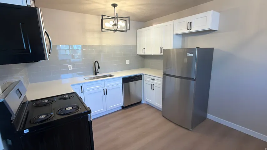 Kitchen with stainless steel appliances, white cabinetry, tasteful backsplash, and light wood-type flooring