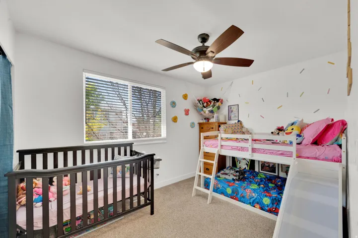 Bedroom with a nursery area, light carpet, and a ceiling fan