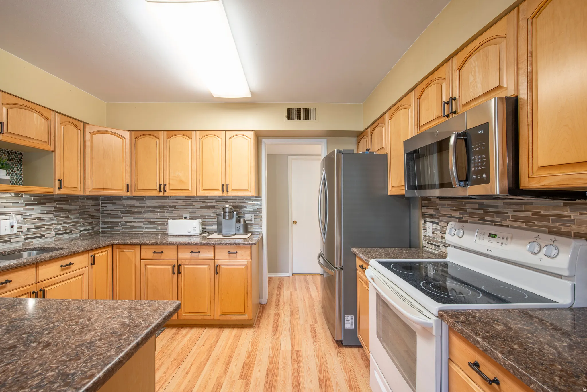 Kitchen with white electric range oven, stainless steel microwave, dark stone counters, light wood finished floors, and decorative backsplash