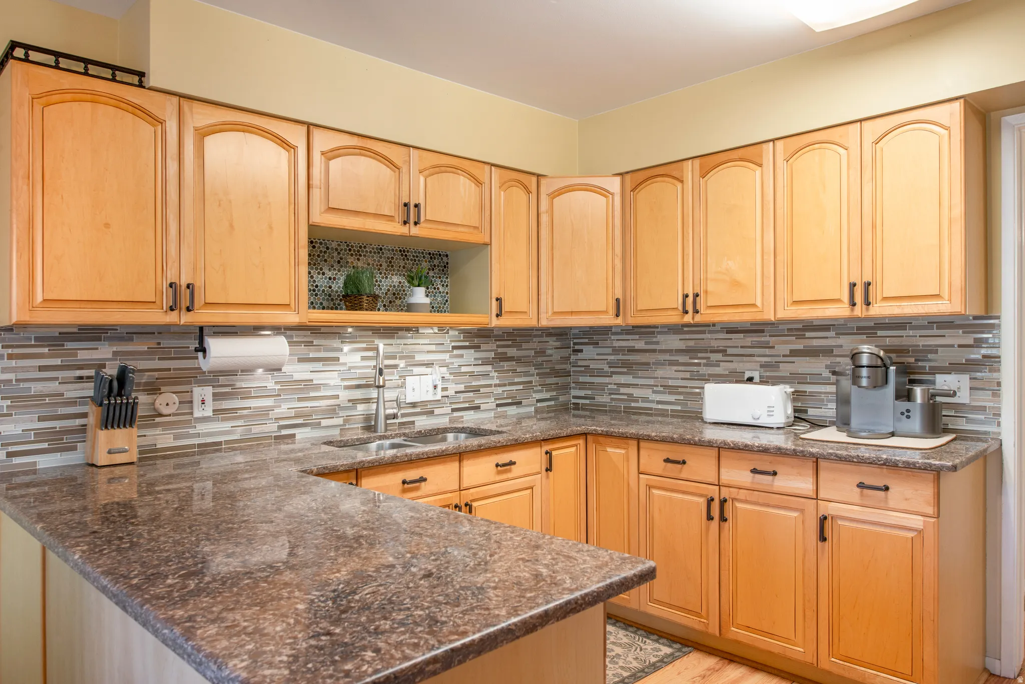 Kitchen with light wood finish cabinetry, dark stone counters, and a peninsula