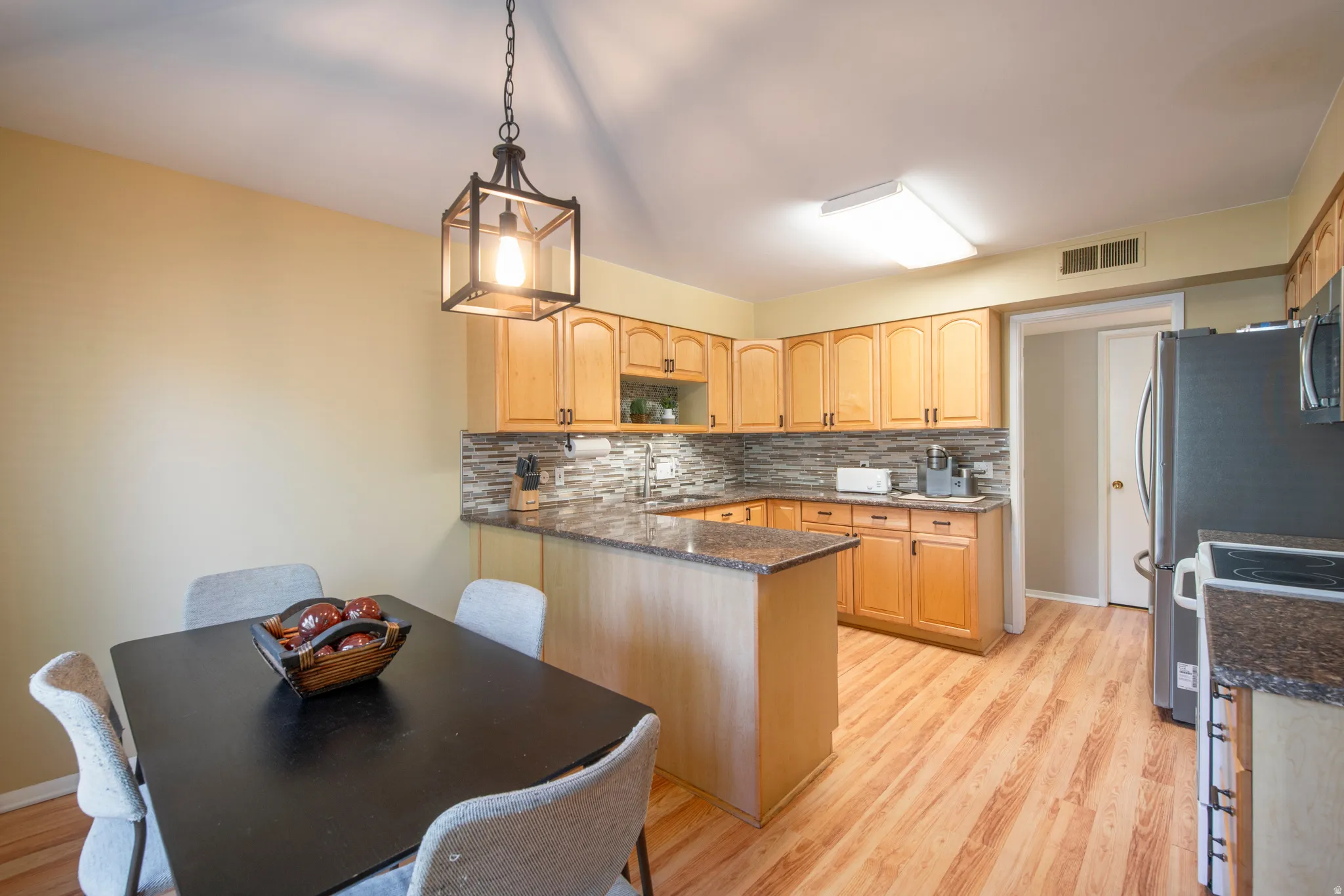 Kitchen with light wood-type flooring, tasteful backsplash, dark stone counters, a peninsula, and open shelves