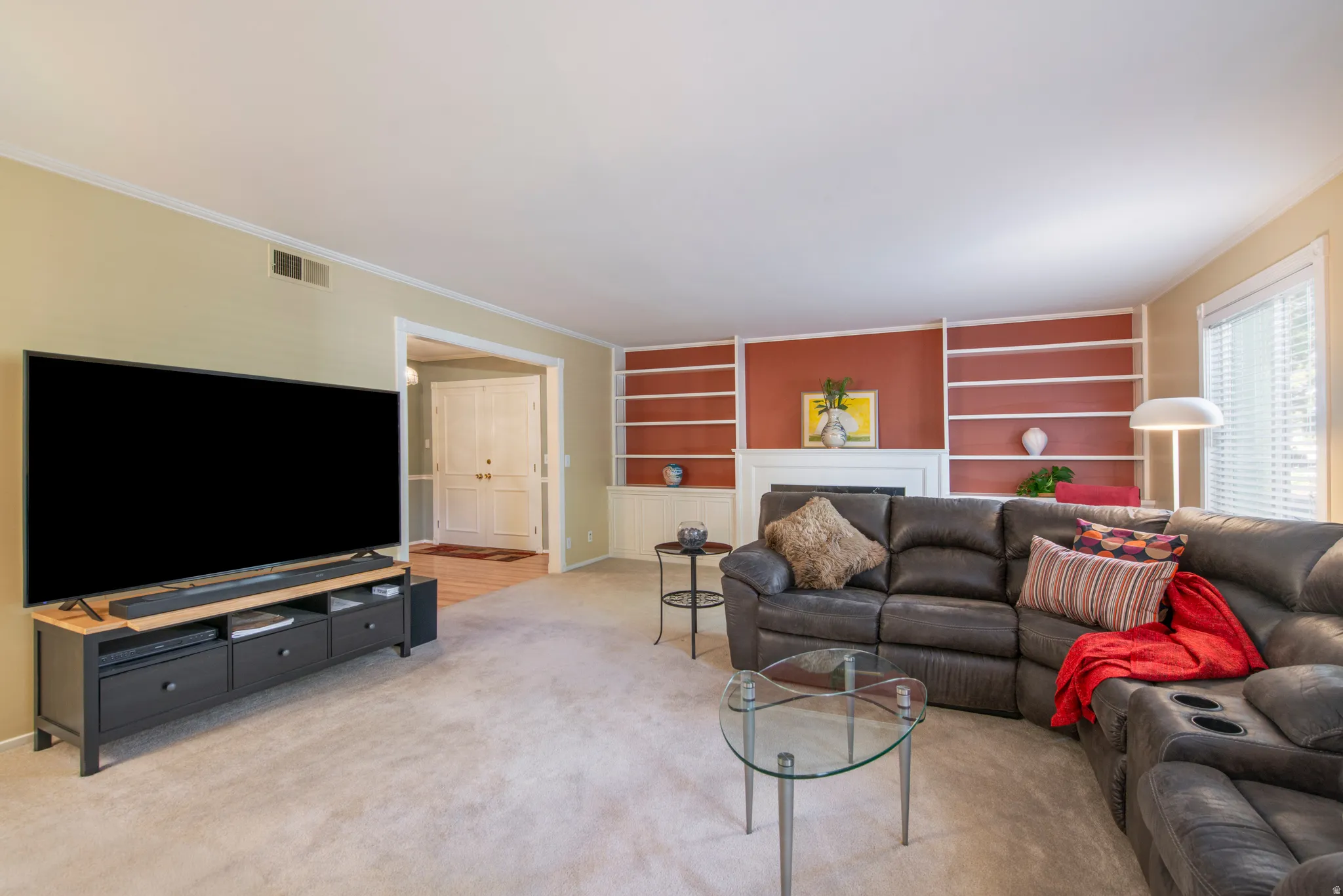 Living area with built in shelves, ornamental molding, light carpet, and a fireplace