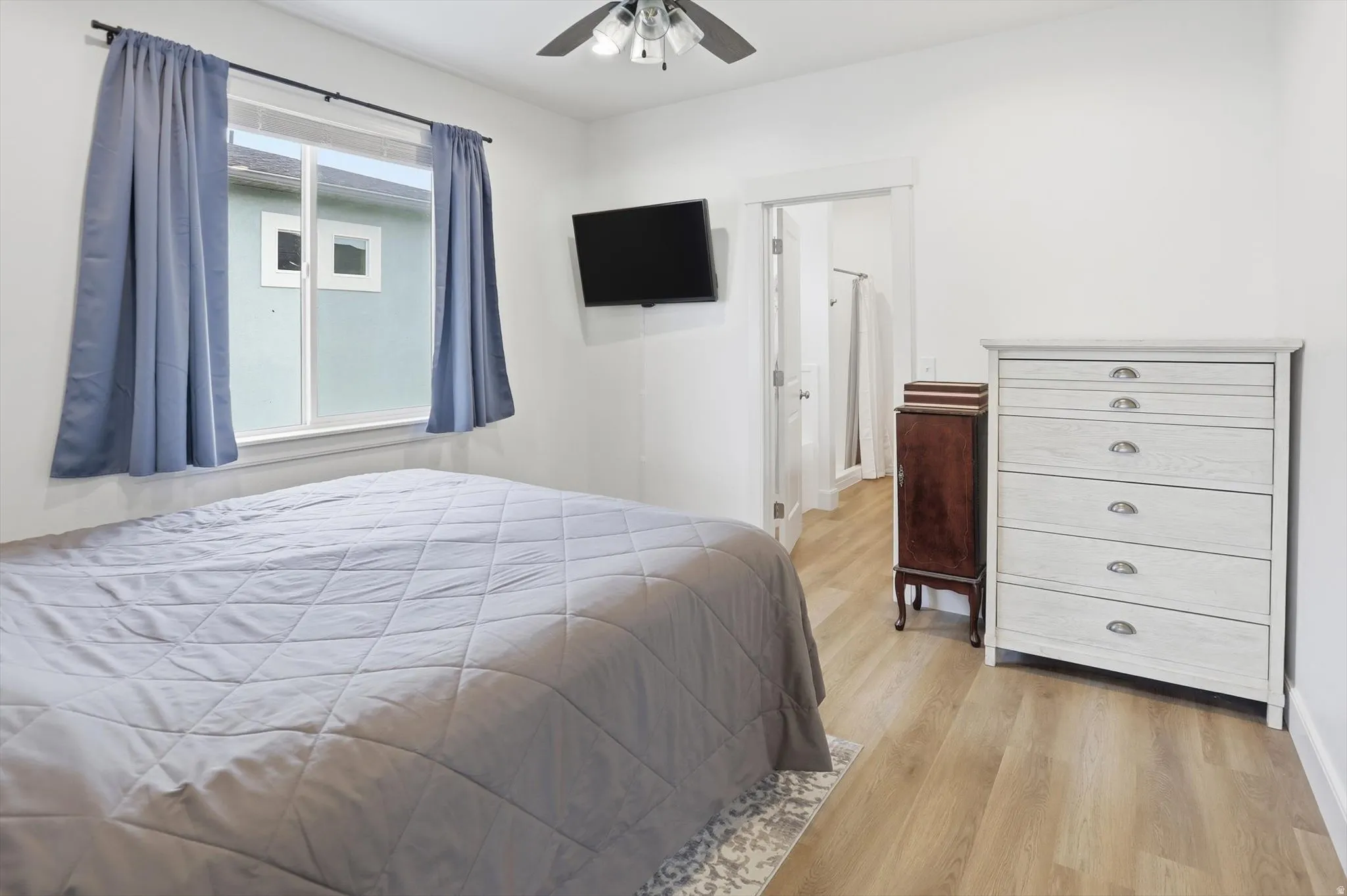 Bedroom with light wood-style floors, ceiling fan, and ensuite bathroom