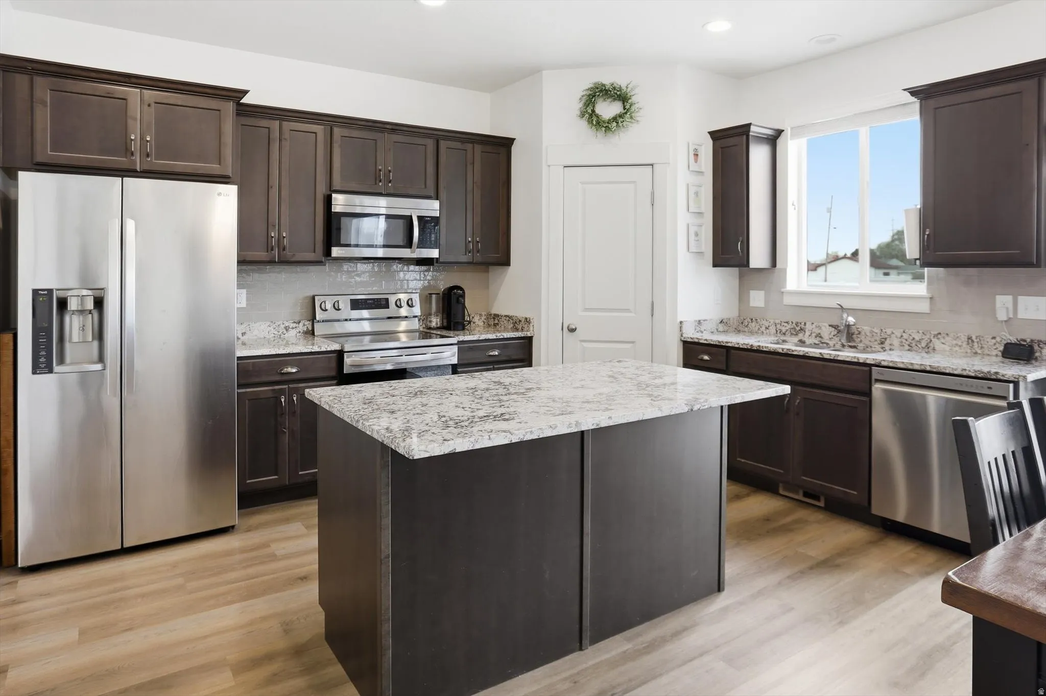 Kitchen featuring stainless steel appliances, dark wood finish cabinets, light wood-style flooring, a center island, and recessed lighting