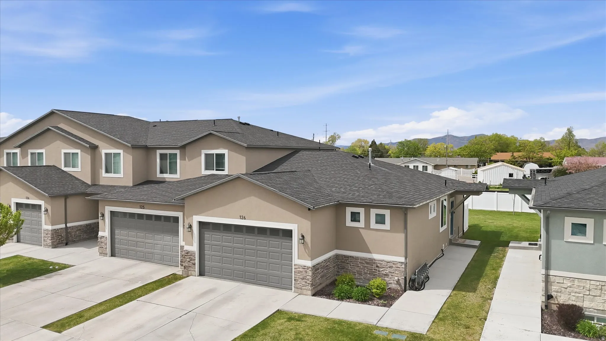 View of front facade with stone siding, stucco siding, concrete driveway, a shingled roof, and a residential view