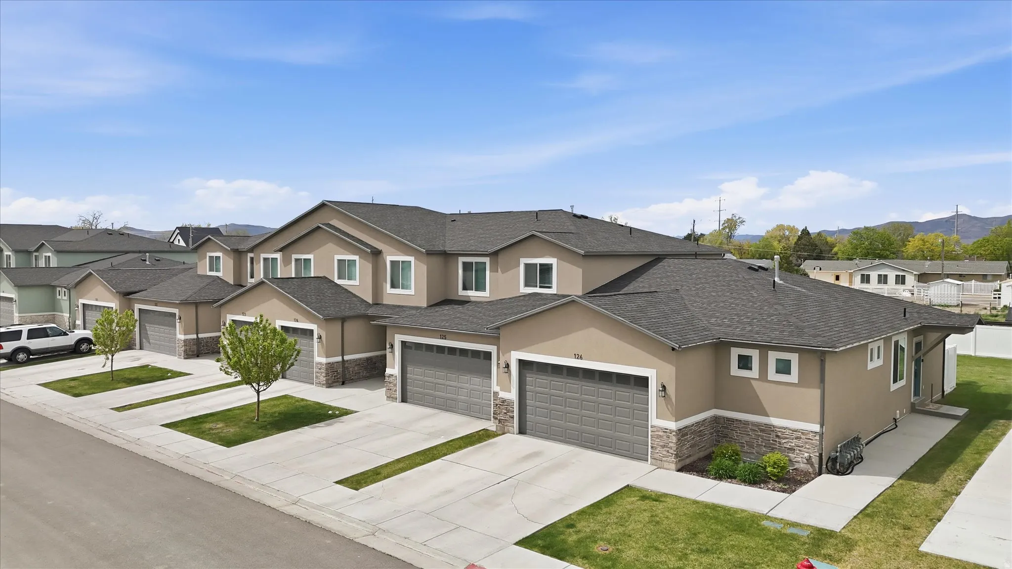 Traditional-style home with stucco siding, stone siding, a residential view, driveway, and roof with shingles