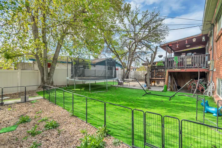 Fenced backyard with a trampoline, a deck, a patio area, and a gate