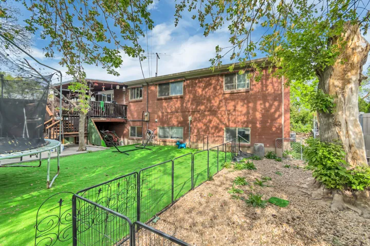 Back of house with a trampoline, a fenced backyard, a deck, a gate, and brick siding