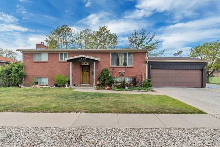 Raised ranch featuring brick siding, a garage, driveway, a front lawn, and a chimney